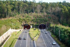 Aerial view of the twin bores of the Hindhead Tunnel on the A3, surrounded by wooded hillside, with vehicles travelling through both directions