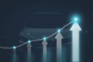 A rising line chart with glowing blue data points and a series of white upward-pointing arrows of increasing height, overlaid on a blurred image of a car's bonnet against a dark blue background, symbolising upward revenue and profit growth