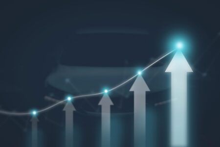 A rising line chart with glowing blue data points and a series of white upward-pointing arrows of increasing height, overlaid on a blurred image of a car's bonnet against a dark blue background, symbolising upward revenue and profit growth