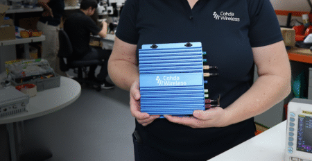 Cohda’s V2X on-board unit earns OmniAir certification in US A blue Cohda Wireless branded on-board unit being held by an employee
