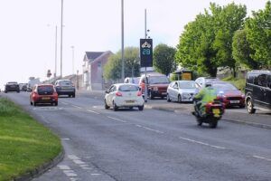 A vehicle activated sign at the roadside in Swansea, displaying a speed reading and an "ARAF SLOW" warning to an approaching motorcyclist