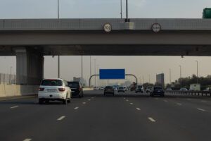 Traffic travelling along a multi-lane motorway in Abu Dhabi, passing beneath an overpass marked with speed and height restriction signs.