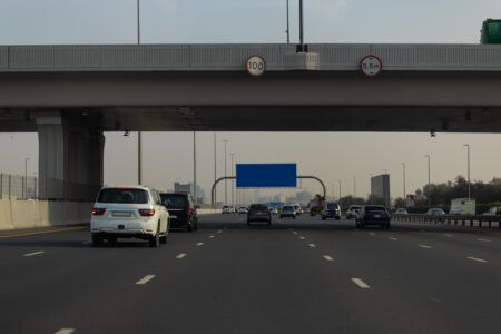 Q Mobility activates paid parking in three Al Ain sectors Traffic travelling along a multi-lane motorway in Abu Dhabi, passing beneath an overpass marked with speed and height restriction signs.