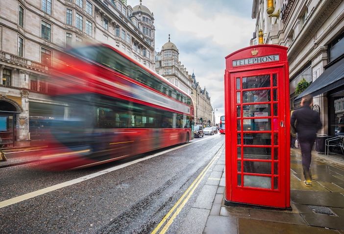 London, England - Iconic blurred red double-decker bus on the move with traditional red telephone box in the center of London at daytime