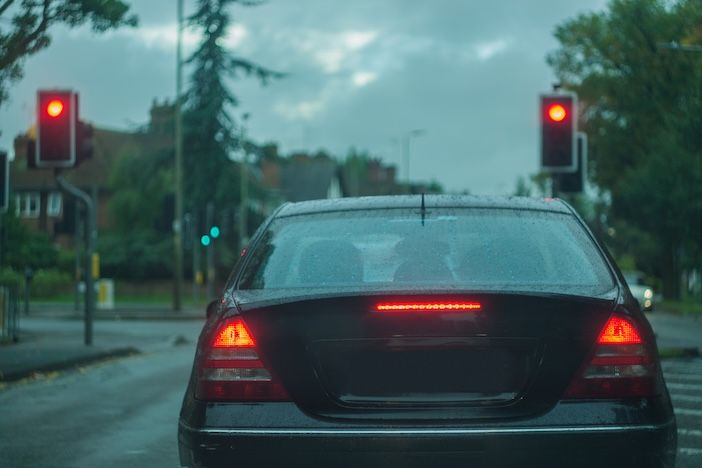 Sensys Gatso wins Queensland red light camera upgrade contract Rear view of a car, displaying stop ligths and red lights, traffic signals, at dusk, in poor visibility conditions. Concept photo, with shallow depth of field and toned colors.