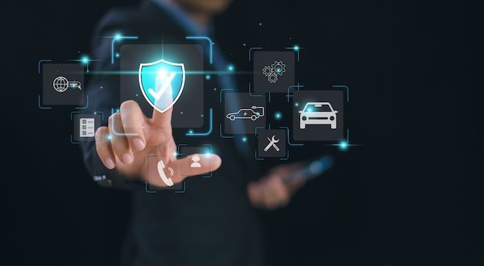 A person in a dark suit touches a glowing blue shield icon with a tick, surrounded by floating icons including a car, a tow truck, a wrench and a globe.