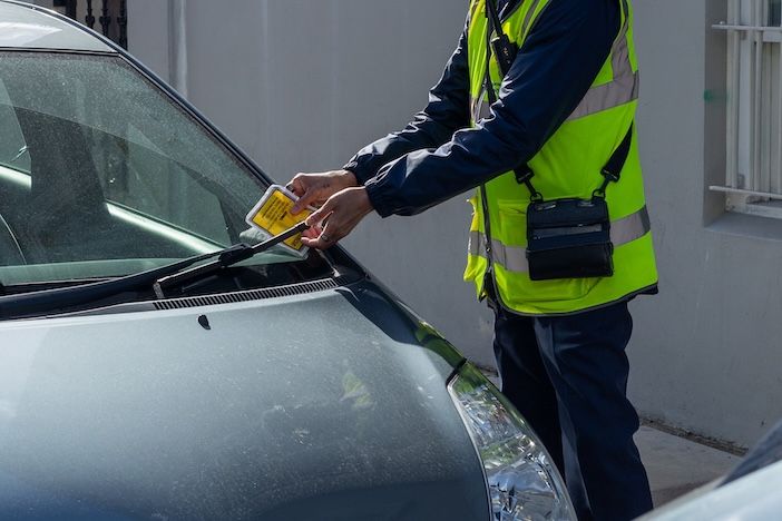 APCOA acquires UK Parking Patrol to expand enforcement offer A person in a high-visibility vest placing a yellow notice under the windscreen wiper of a grey car.