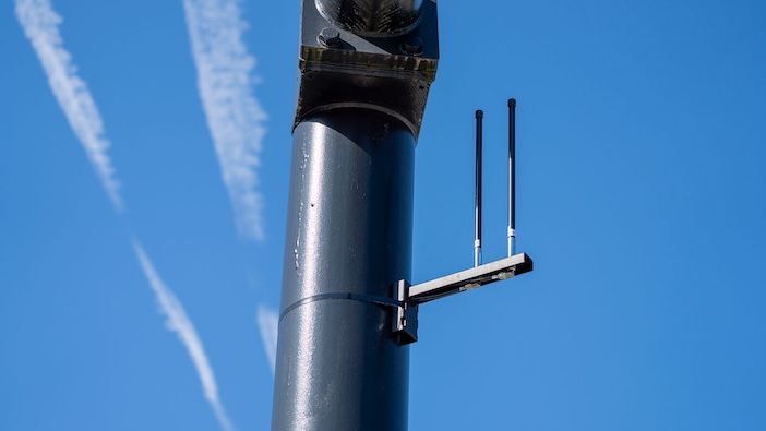 Close-up of a dark metal pole against a blue sky, with two thin black antennas on a horizontal bracket near the top.
