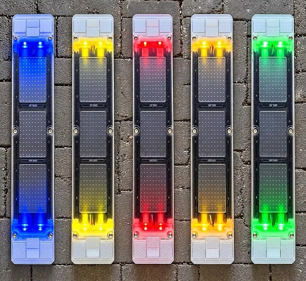 Five long, narrow devices lie side by side on dark cobbled paving, each with solar panels and lights glowing blue, yellow, red, amber and green.